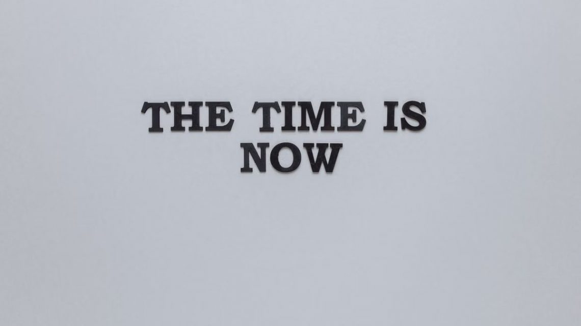 Minimalist poster with the motivational quote 'The Time is Now' on a gray background.