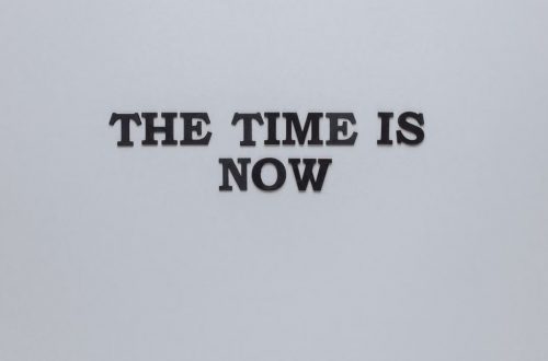 Minimalist poster with the motivational quote 'The Time is Now' on a gray background.